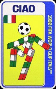 Ciao, mascota oficial del Mundial Italia 1990, que representa un cuerpo geométrico, compuesto por cubos de colores verde, blanco y rojo, en distintas posiciones para crear la forma de una figura humana con piernas, brazos y torso, que se encuentra en una posición dinámica, con los brazos extendidos lateralmente, una pierna flexionada hacia arriba, y la otra extendida hacia el suelo. La cabeza de la figura es un balón de fútbol en blanco y negro.