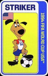 Striker, mascota oficial del Mundial EE.UU. 1994, que representa a un perro antropomórfico y caricaturesco de color marrón, con las orejas y nariz negras, que sonríe mientras posa con una de sus patas calzadas con botines negros, sobre un balón de fútbol. Va vestido con pantaloncillos azules, camisa y calcetas blancas con detalles en rojo, y, sobre el pecho, la leyenda "USA 94".