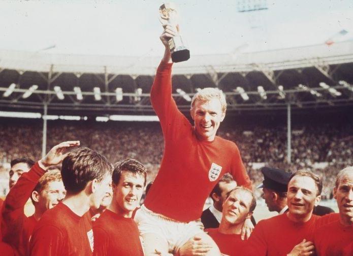 Un sonriente capitán de la selección de Inglaterra de fútbol, Bobby Moore, levanta con su brazo derecho la copa Jules Rimet, tras haber vencido, en tiempo extra, a Alemania Occidental por 4-2, en la Final de la Copa del Mundo de la FIFA de 1966, celebrada el 30 de julio de 1966 en el estadio londinense de Wembley. Moore es llevado en hombros por sus compañeros de equipo, entre los que se encuentran, de izquierda a derecha, Gordon Banks, Alan Ball, Roger Hunt, Geoff Hurst, Ray Wilson, George Cohen y BobbY Charlton.