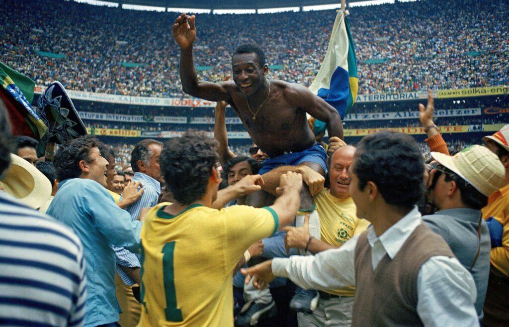 Pelé, sin camiseta, sonriente y con un brazo en alto, es levantado en hombros por sus compañeros de equipo y otras personas después de ganar la final de la Copa del Mundo de la FIFA México 1970 en el Estadio Azteca de la Ciudad de México.